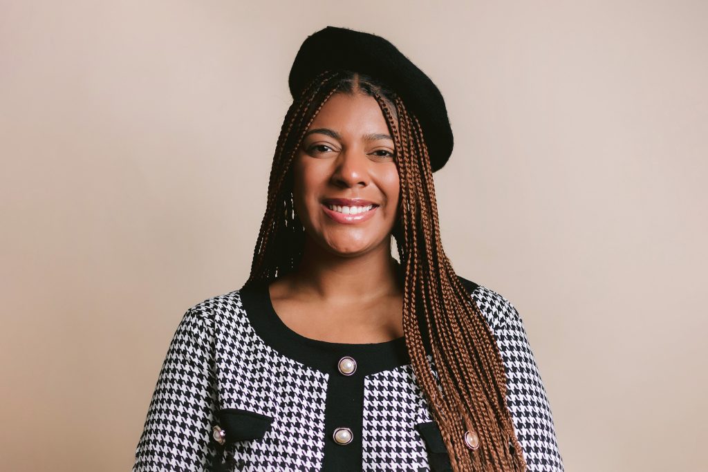 a professional headshot of a woman with braids, wearing a stylish black hat, exuding confidence and elegance.