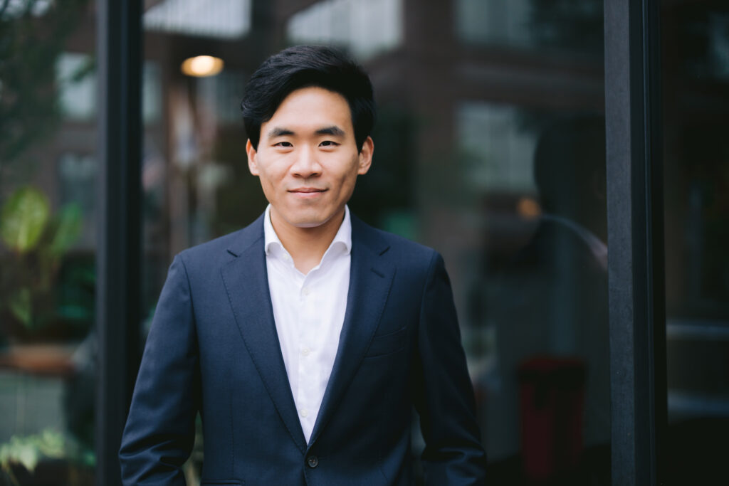 a young male realtor in a suit and tie stands outside, posing confidently for a realtor branding photo session.