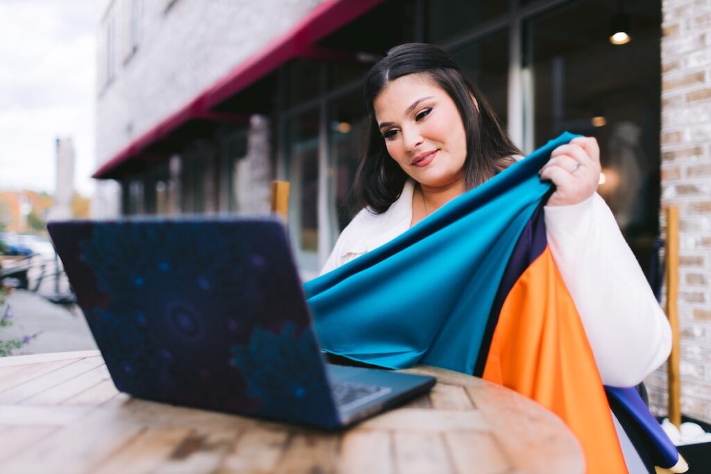 a female wedding planner sits at a table with a laptop, showcasing fabric swatches to her client in a personal branding session.