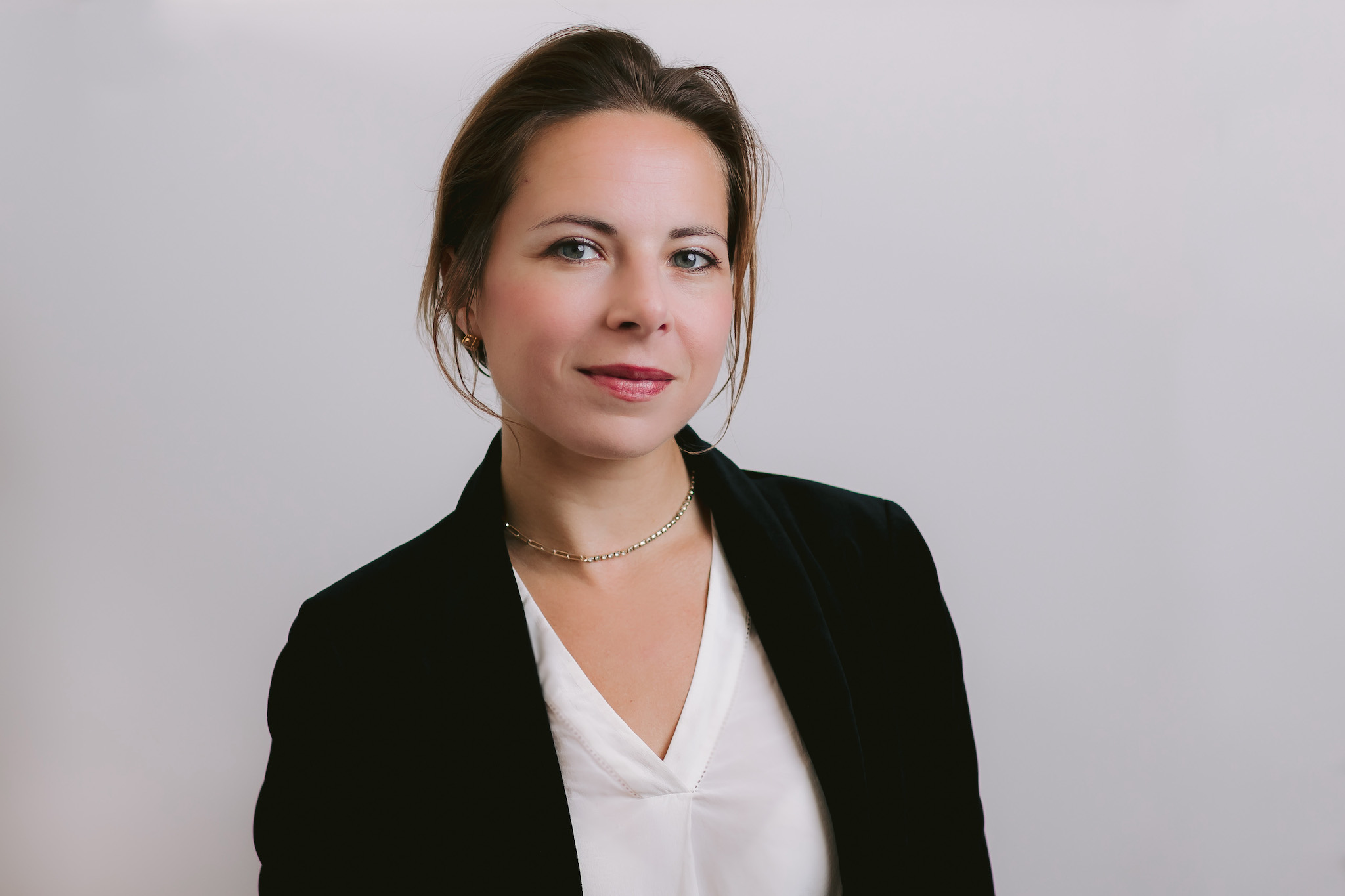 a female professional in a black blazer and white shirt poses for a professional headshot, showcasing her polished and confident look.