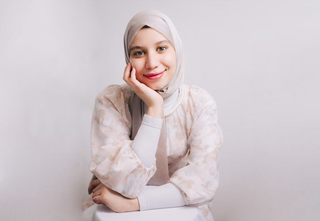 a smiling woman in a hijab poses confidently for a professional headshot, radiating warmth and professionalism.