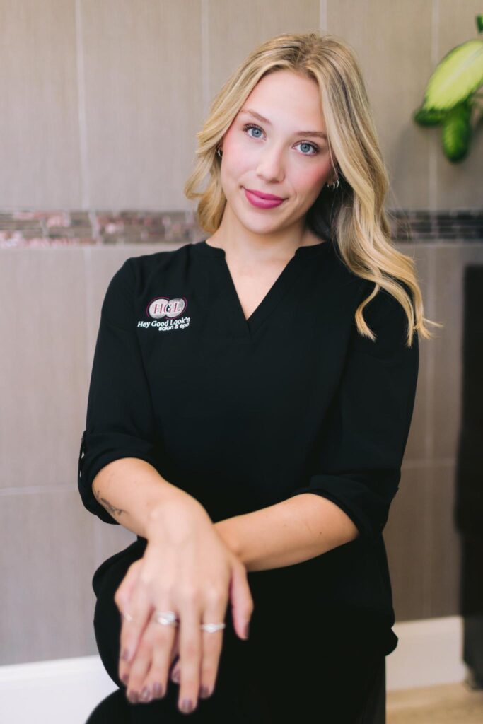 a woman dressed in a black shirt sits on a chair, presenting a polished and professional image in her professional headshot.