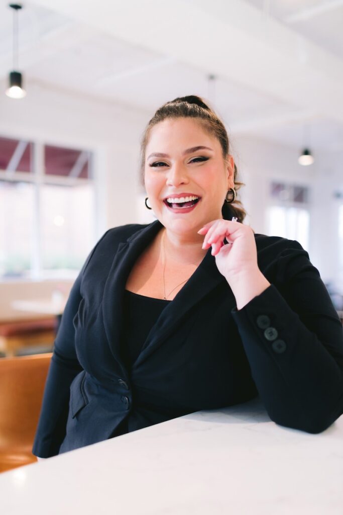 a confident female entrepreneur in a business suit smiles warmly posing for a personal branding shoot at a cafe.
